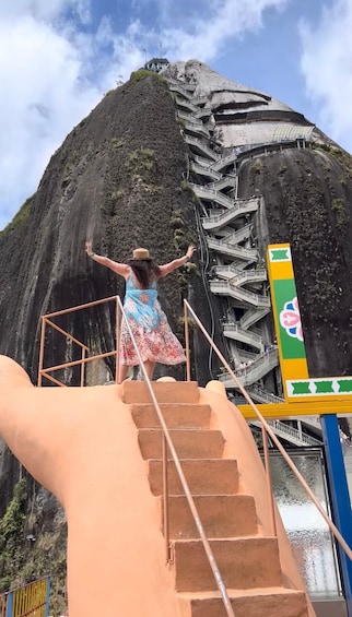 A person standing on a staircase with arms outstretched, overlooking a large rock formation. 4