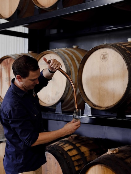 A person holding a glass and a copper pipe, likely in a winery or distillery. 1