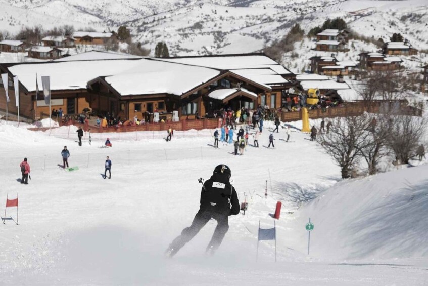 A skier descending a snowy slope with a lodge in the background. 3