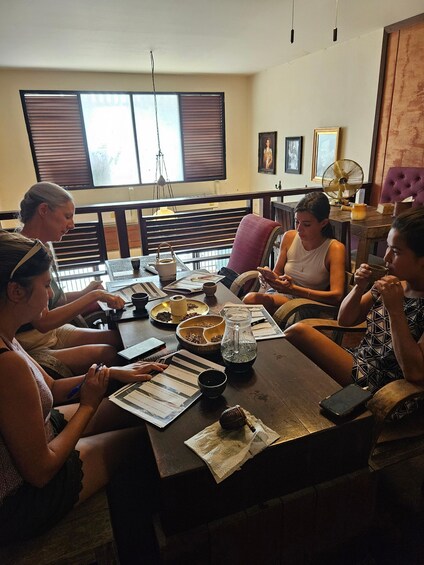 A group of people sitting around a table with various items like a pitcher, cups, and papers. 4