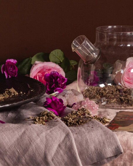 A glass container with dried herbs, a black plate with a flower, and a pink rose. 5