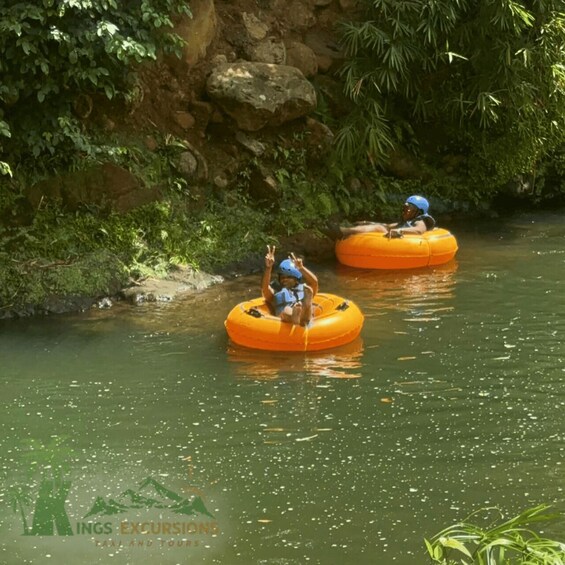 Two people on inflatable tubes in a river surrounded by greenery. 2