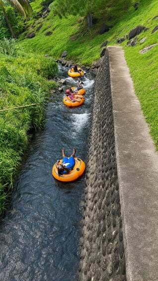 People in orange rafts navigating a narrow water channel flanked by grassy banks and a concrete wall. 3