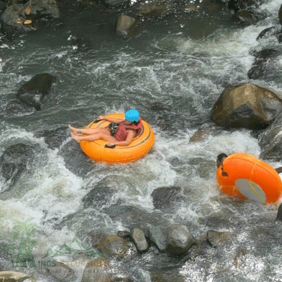 A person in a blue helmet and red life jacket floating on an orange raft in a river with rocks. 4