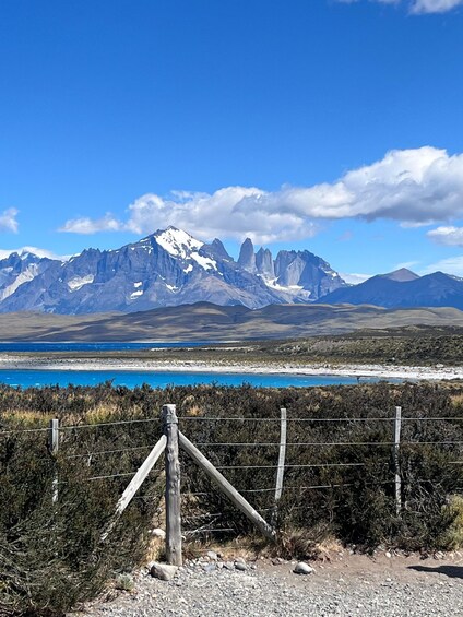A mountainous landscape with a clear blue sky, a body of water, and a wooden fence in the foreground. 3