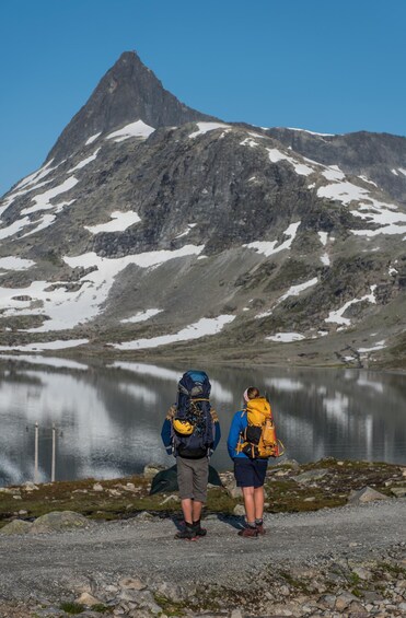 Two hikers with backpacks standing by a lake with a mountain in the background. 5