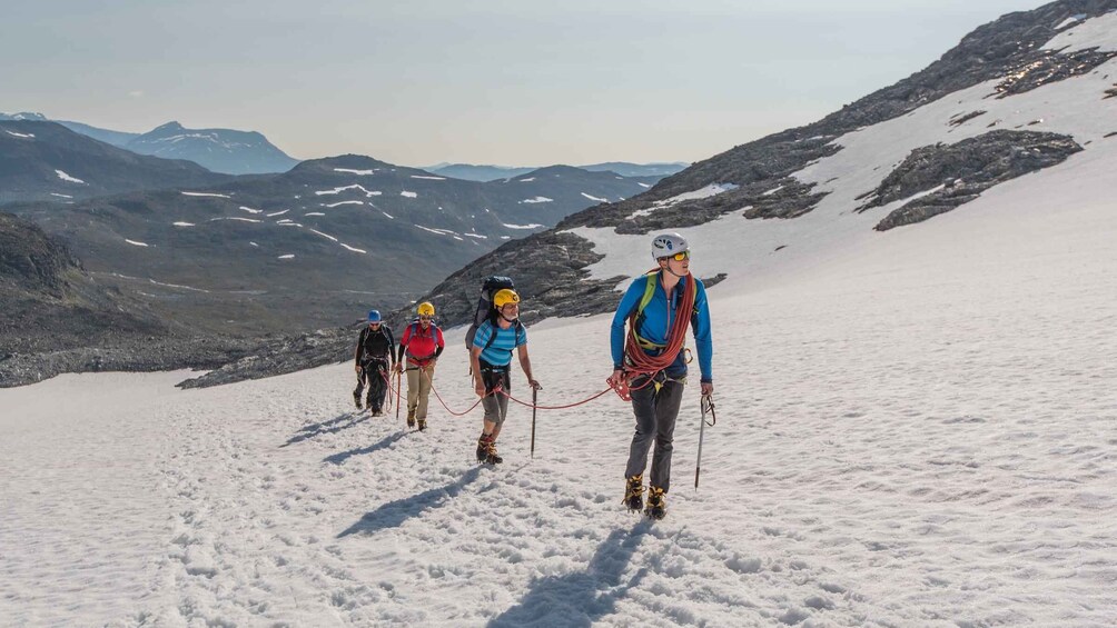 A group of climbers ascending a snowy mountain with rocky terrain and distant mountains in the background. 4