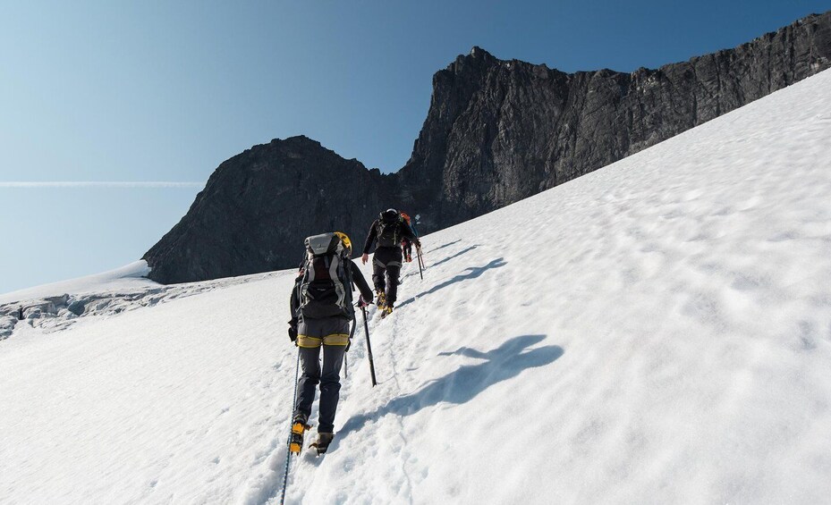 A group of hikers ascending a snow-covered mountain slope with rocky cliffs in the background. 3