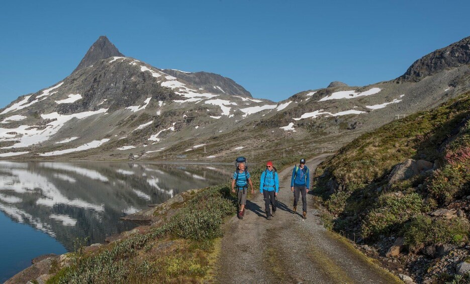 A mountain path with hikers, a lake, and a prominent peak. 1