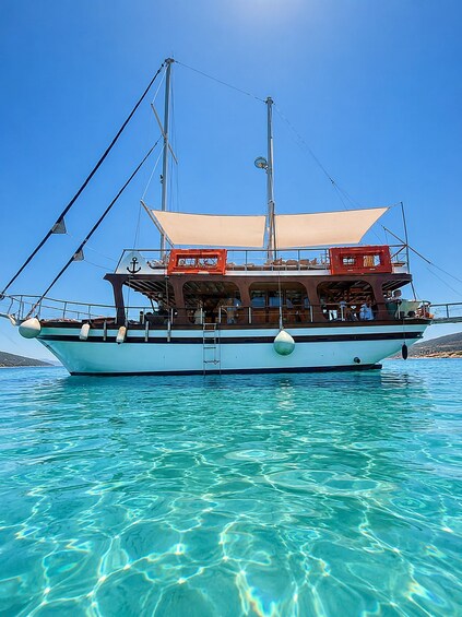 A boat with a cabin and a sail, floating on clear blue water. 4