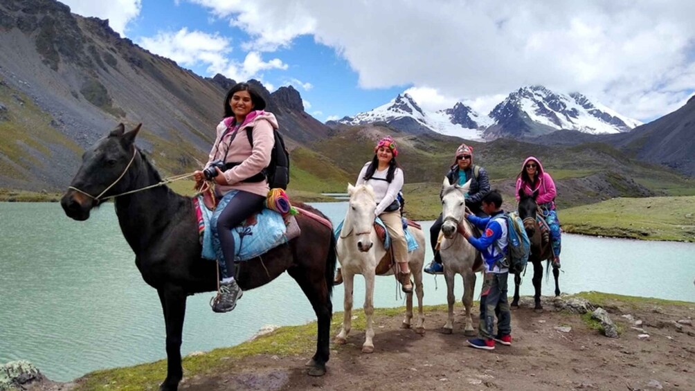 A group of people on horseback by a lake with mountains in the background. 2