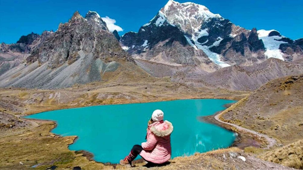 A person sitting by a turquoise lake with mountains in the background. 4
