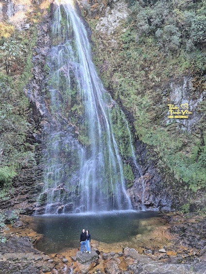A waterfall cascading into a clear pool surrounded by rocky terrain and dense greenery. 4