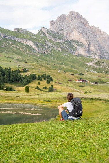 A person sitting on grass near a lake with mountains in the background. 3