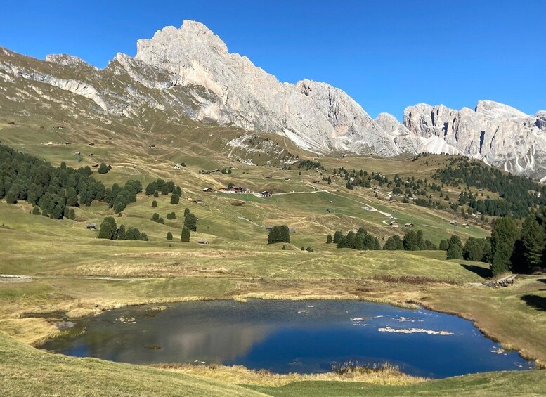 A mountainous landscape with a pond, scattered trees, and a few buildings. 1
