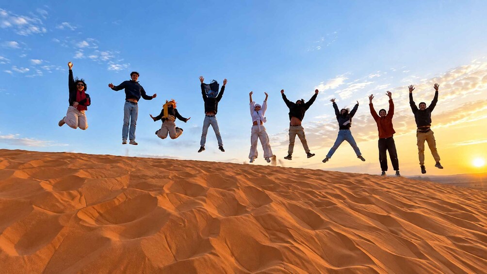A group of people jumping in the desert at sunset. 1