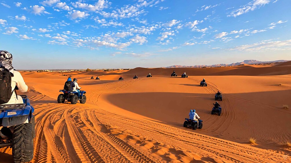 A group of people riding quad bikes on sand dunes under a clear sky. 4