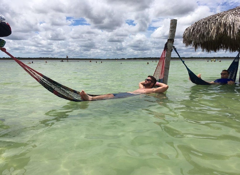 A person relaxing in a hammock in clear water, with a thatched roof structure nearby. 1