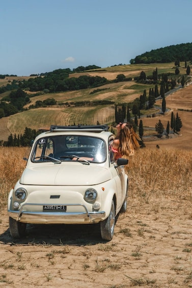 A white vintage car parked on a dirt road with a woman leaning out of the window. 5