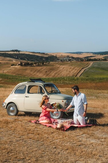 A vintage car parked in a field with a picnic setup. 4