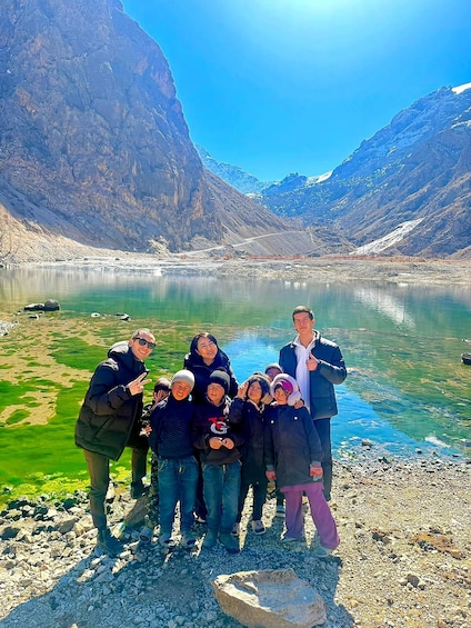 A group of people standing by a clear lake with mountains in the background. 2