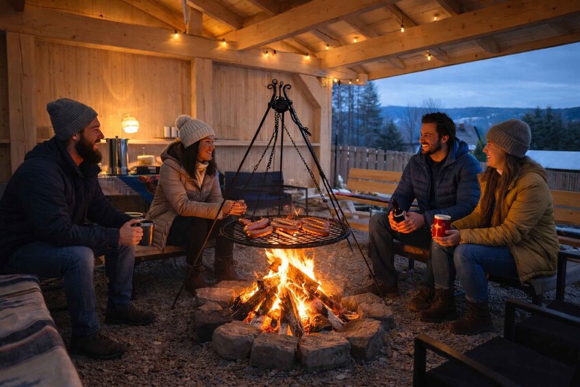A group of people sitting around a campfire in a wooden outdoor setting. 2
