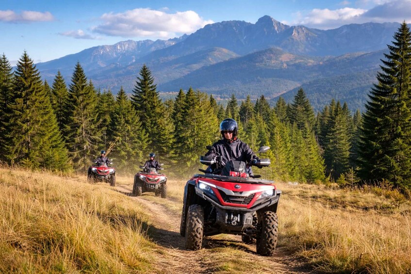 Three riders on ATVs on a dirt trail with a mountainous backdrop. 5