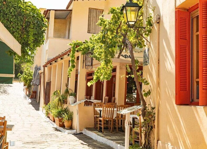 A narrow cobblestone street lined with buildings, outdoor seating, and potted plants. 4