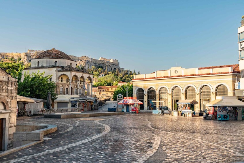 A cobblestone square with historic buildings, a dome, and a hill with ruins in the background. 1