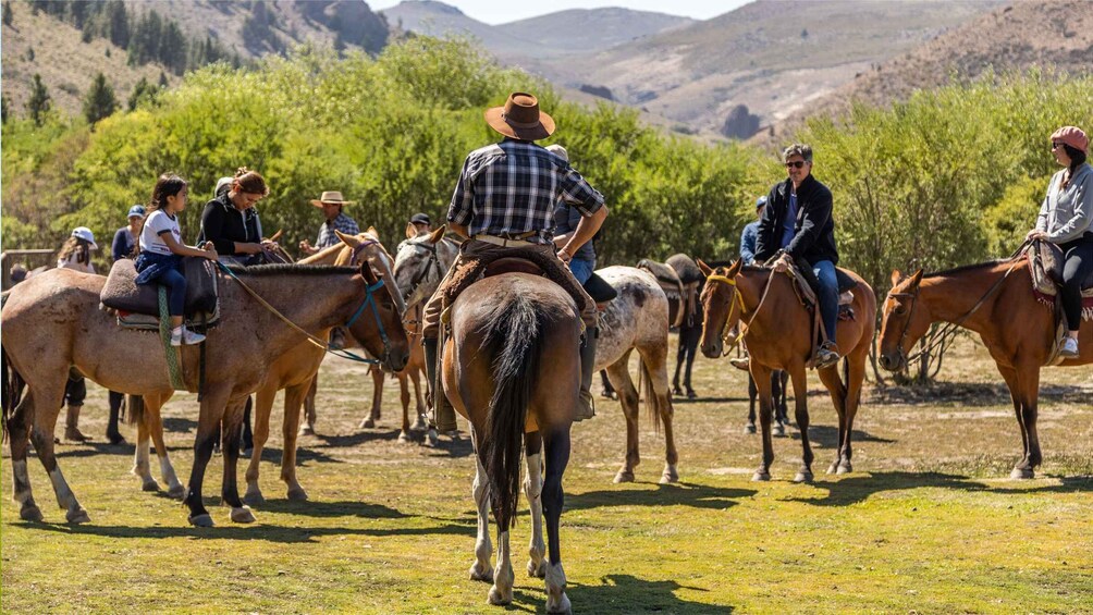 A group of people riding horses in a grassy field with mountains in the background. 2
