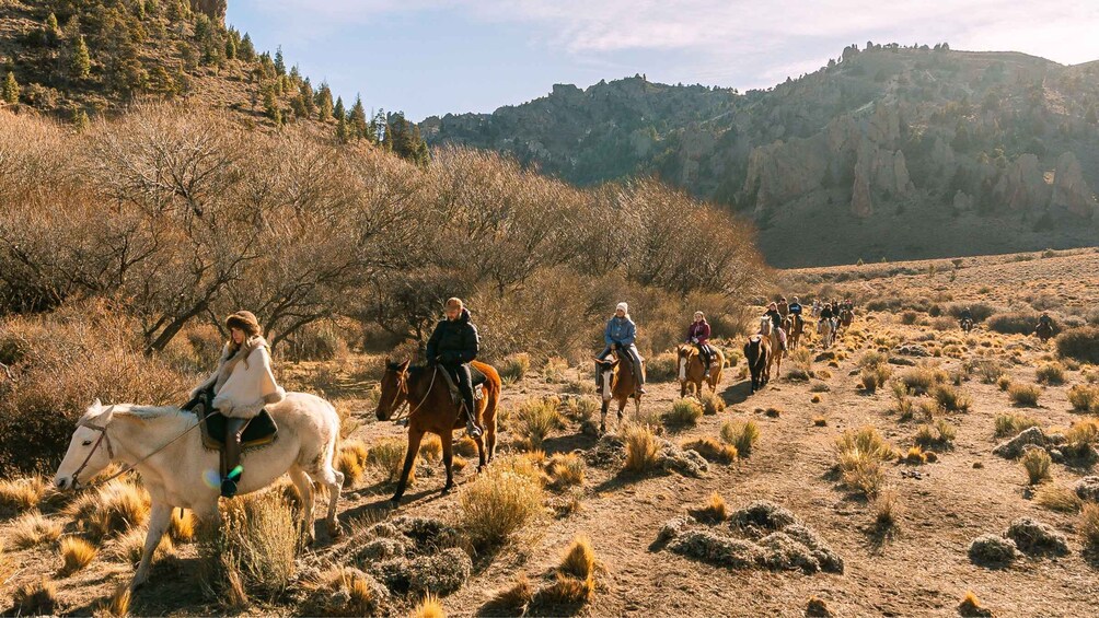 A group of people horseback riding along a dry, hilly terrain with sparse vegetation and rocky outcrops. 4