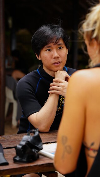 A person sitting at a wooden table with a camera and a notebook. 3
