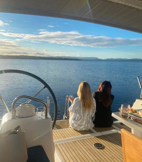 Two people on a boat deck overlooking a calm body of water with a distant shoreline. 1