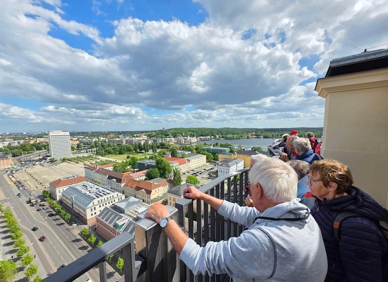 A group of people on a balcony overlooking a cityscape with buildings, a river, and a clear sky. 2