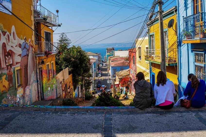 A narrow street with colorful buildings, a mural, and a clear view of the sea. 1