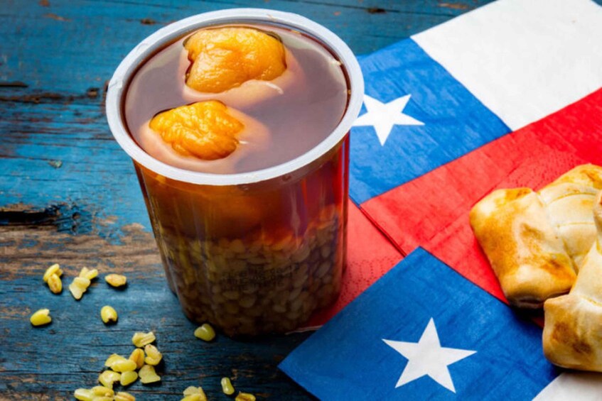 A cup with a beverage and two oranges, a Texan flag, and a piece of food on a wooden surface. 4