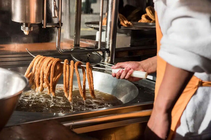 A person frying churros in a deep fryer. 3