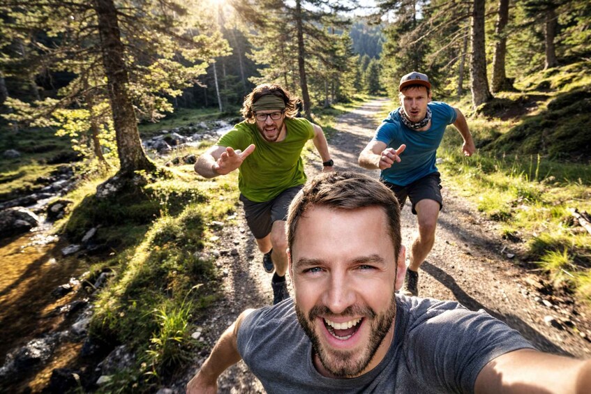 Three people running on a forest trail with sunlight filtering through the trees. 1