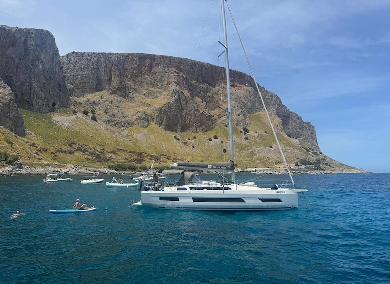 A sailboat anchored near a rocky coastline with cliffs in the background. 3