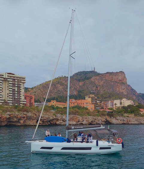 A sailboat named DUFOUR on calm waters with a coastal town and a prominent hill in the background. 5