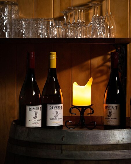 Three bottles of River-T wines on a barrel shelf with a lit candle in the background. 2