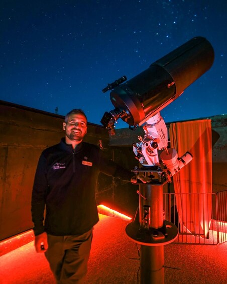 A person standing next to a large telescope with a starry sky in the background. 1