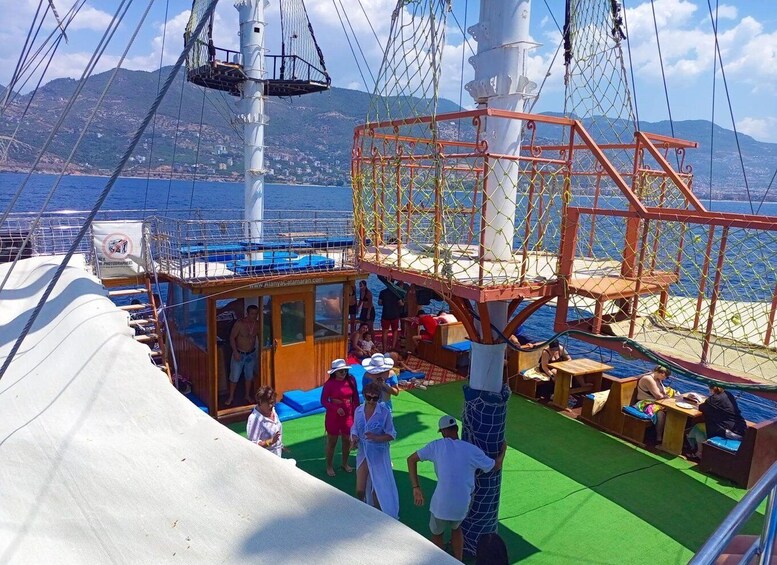 A deck area with people, a netted play structure, and a view of the sea and mountains. 2