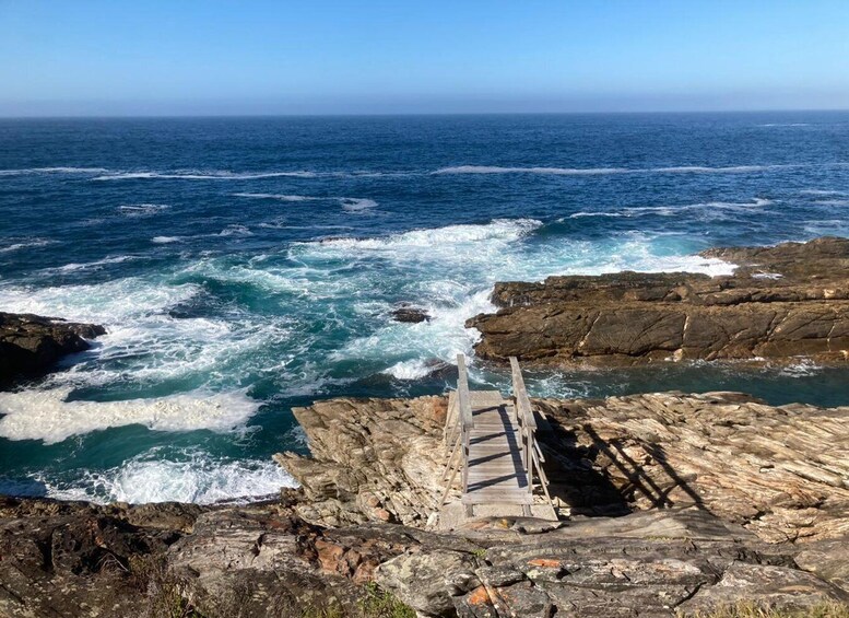 A rocky coastline with waves crashing against the shore and a wooden walkway leading to the water. 3