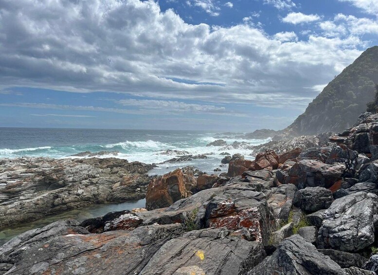 A rocky coastline with waves crashing against the shore under a partly cloudy sky. 2