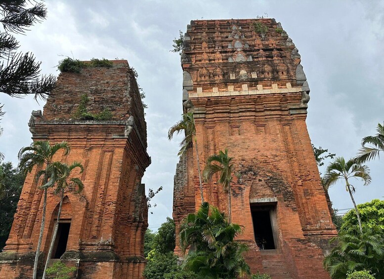 Two ancient brick towers with intricate carvings and a small doorway, surrounded by lush greenery. 1