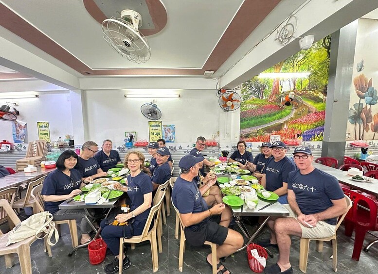 A group of people seated at tables in a room with ceiling fans, a mural, and various posters on the walls. 5