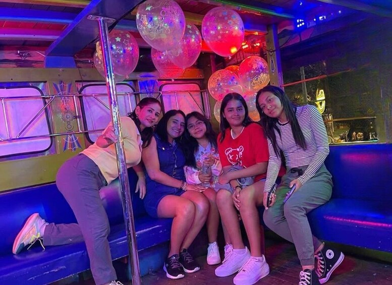 A group of people sitting on a bench in a brightly lit, colorful indoor setting with balloons. 3