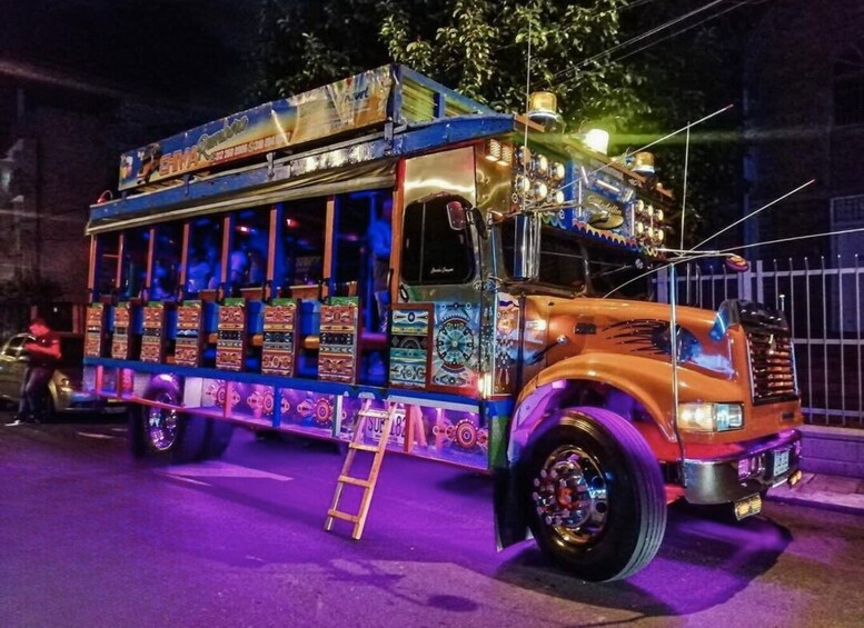 A brightly lit, colorful food truck with a ladder and a person standing beside it. 1
