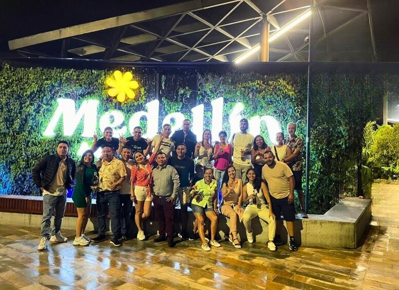 A group of people posing in front of a large illuminated sign with the word 'Medellin' and a flower symbol. 2